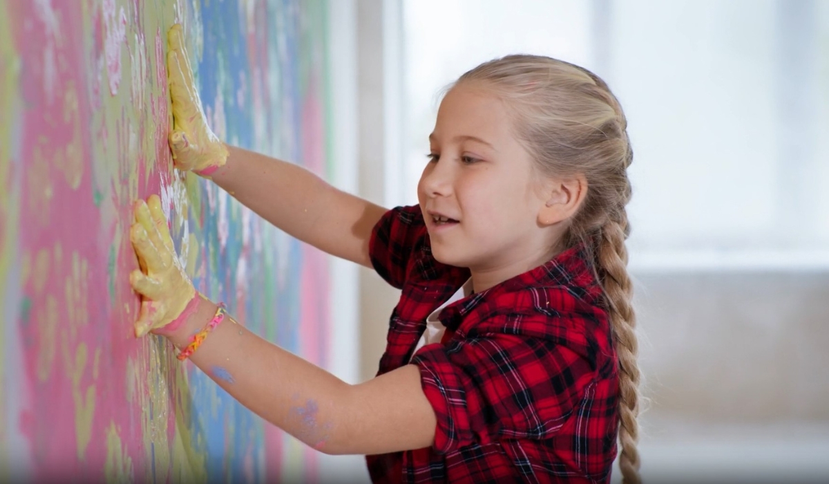 devojčica rukama umazanim od boje ostavlja otiske šaka po zidu