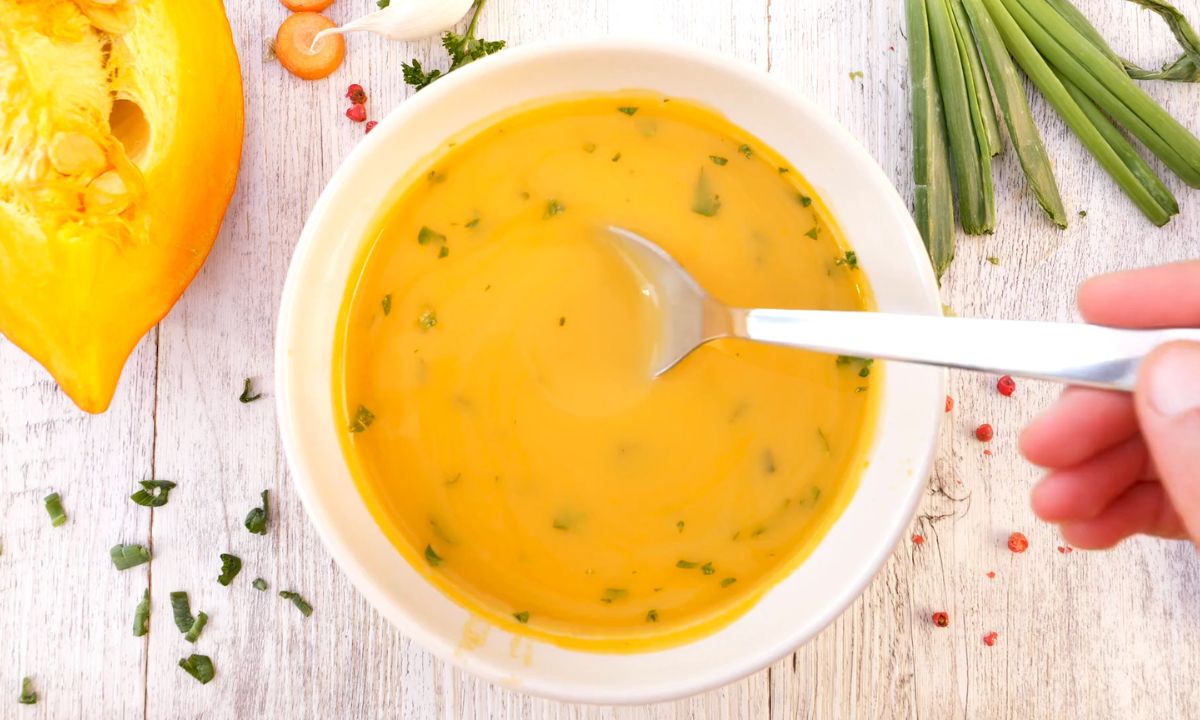 prikaz detoks supe od bundeve na drvenom stolu sa prazilukom u pozadini i peršunom