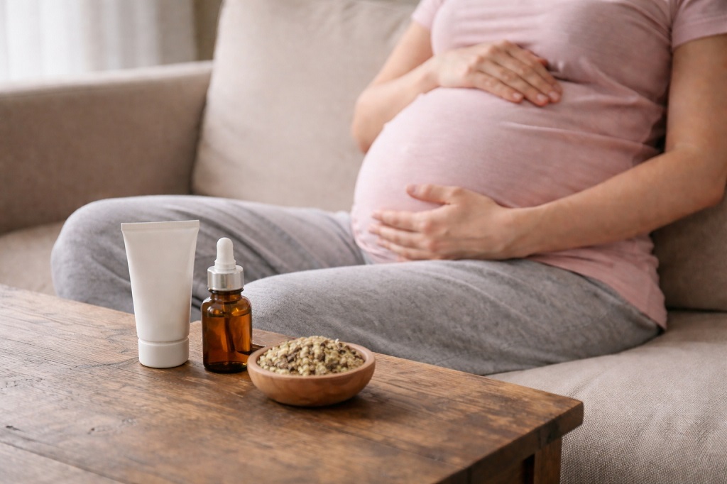 Trudnica sedi na kauฤu pored preparata za negu, meฤu kojima je i najbolji gel za hemoroide kod trudnica