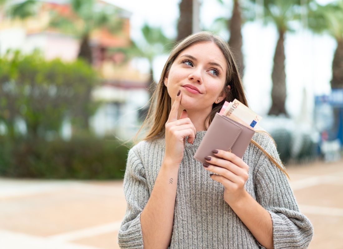 prikaz devojke u prirodi koja drži novčanik u ruci i zamišljeno razmišlja
