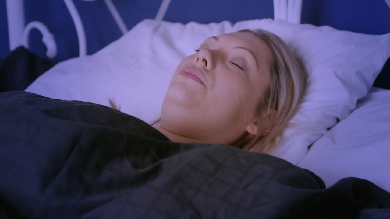 Žena leži na leđima na jastuku i spava u zamračenoj sobi