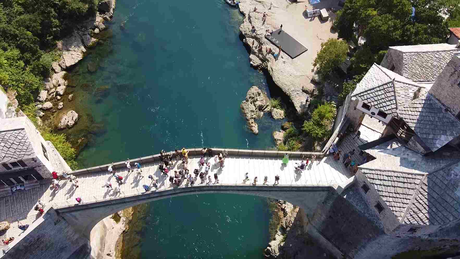 Stari most u Mostaru iz vazduha, sa posetiocima i rekom Neretvom ispod.